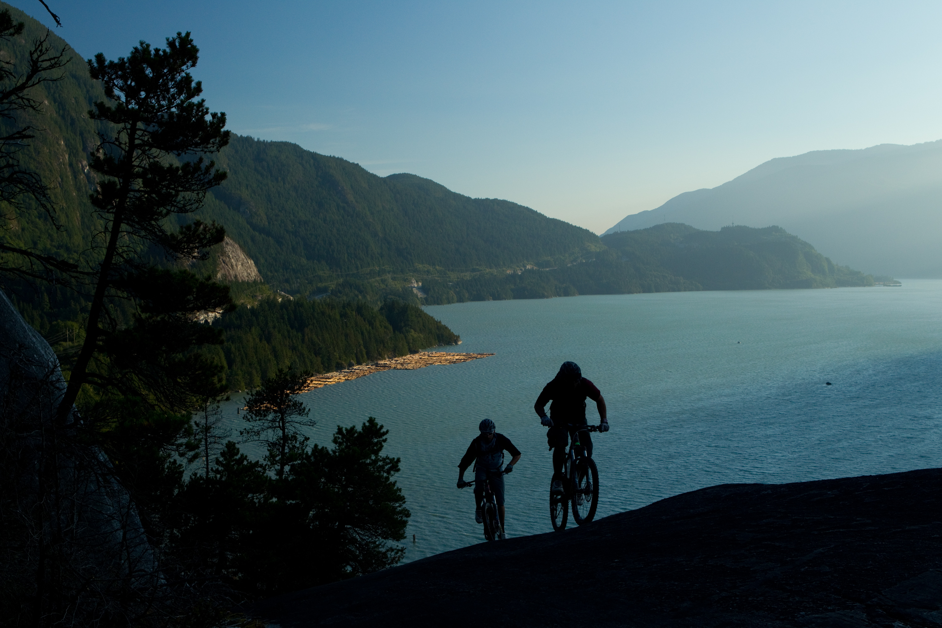 Two riders silhouetted on a slickrock spine with the Sound below