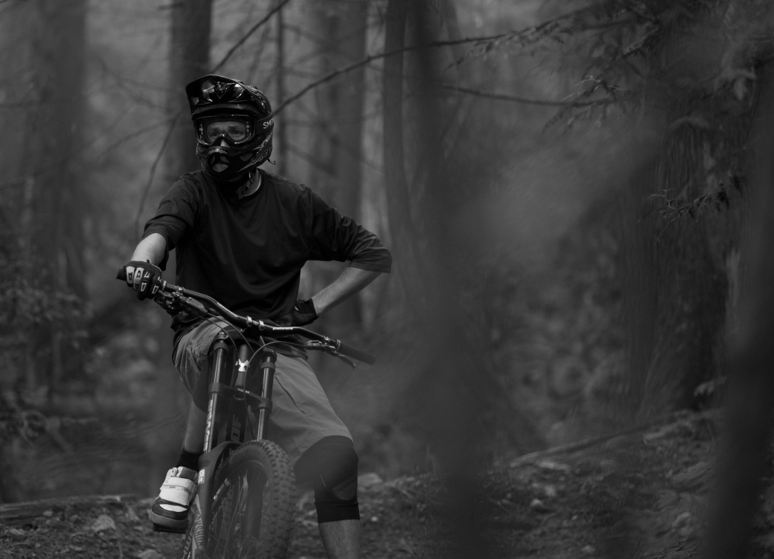 David Watson seated on his mountain bike in the forest, black and white